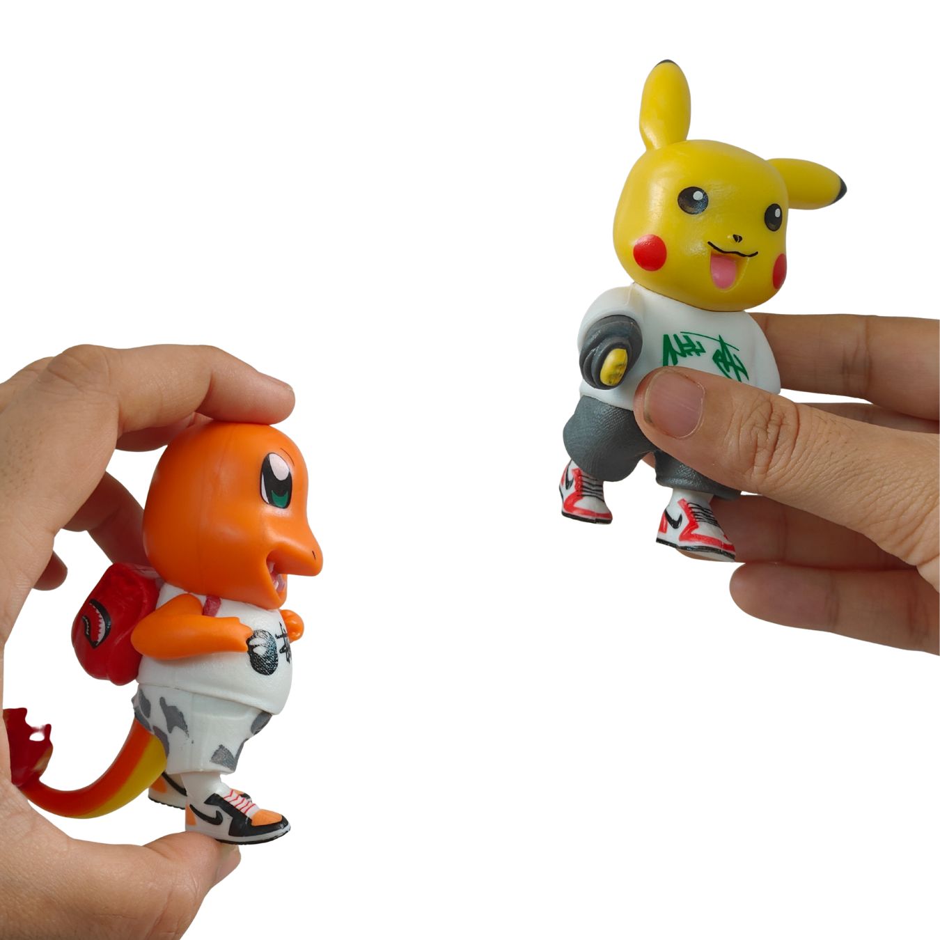 Two small toy figurines being held by human hands against a plain white background: an orange character on the left and a yellow character on the right, both wearing white tops and colorful sneakers.