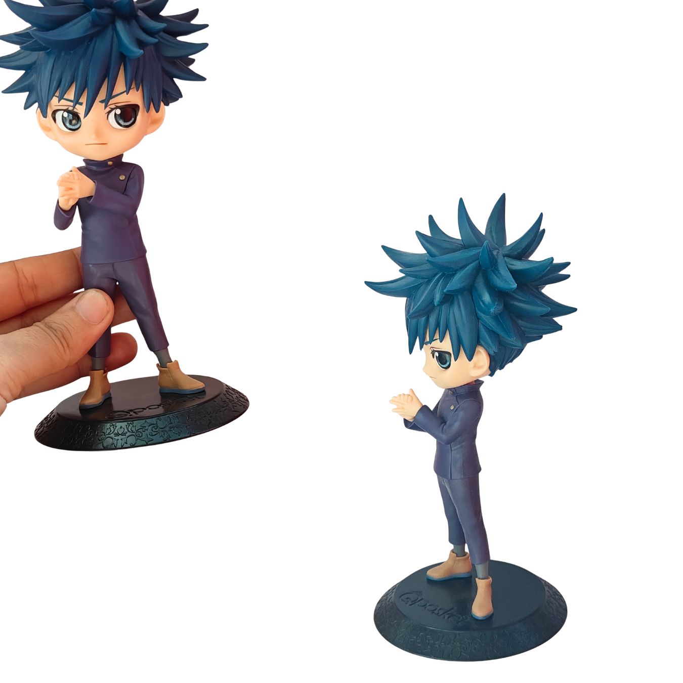 A chibi-style anime figurine of a character with spiky blue hair, wearing a dark purple outfit and brown boots, shown standing on a round base. A human hand is visible holding the figure on the left, while the same figure stands alone on the right against a plain white background.