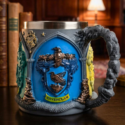 A Ravenclaw themed steel mug with a detailed blue crest, gold eagle, and a sculpted gray dragon handle, set against a blurred library background.