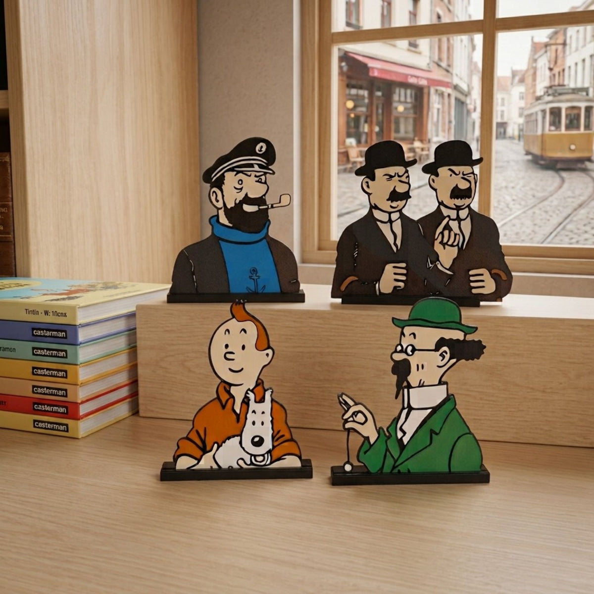 Four cartoon character bookends shaped like Tintin, Captain Nemo, Professor Houdini, and Tintin and Sophie, displayed on a light wood table in front of a window.